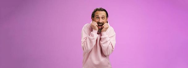 Divertido emocionado jadeando guapo hombre adulto barbudo feliz con capucha rosa encorvado gritando con alegría recibir increíble presente de pie sin palabras emocionado fondo púrpura. Copiar espacio - Foto, imagen