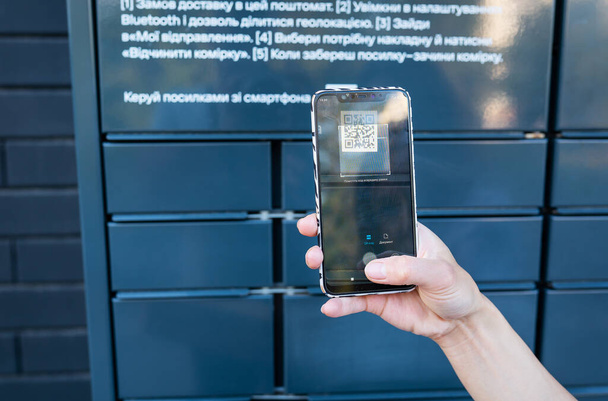 A woman picks up a parcel from a post office by scanning a QR code, online ordering, online shopping. Mail without an employee. Online sales concept - Photo, Image