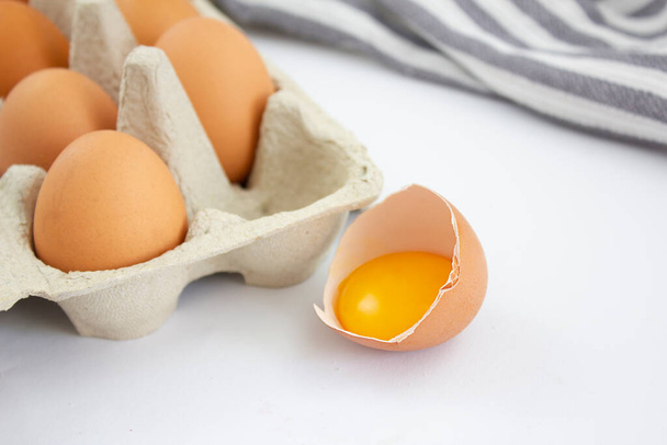 Huevos de pollo frescos en una caja de cartón y un huevo roto sobre un fondo blanco. Copiar espacio. - Foto, imagen