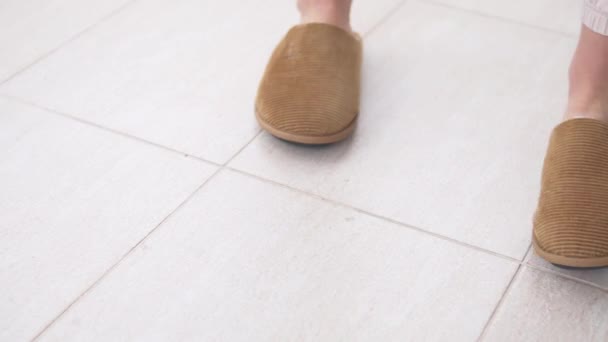 Primo piano, la donna si toglie le pantofole calde sul pavimento piastrellato e se ne va. - Filmati, video