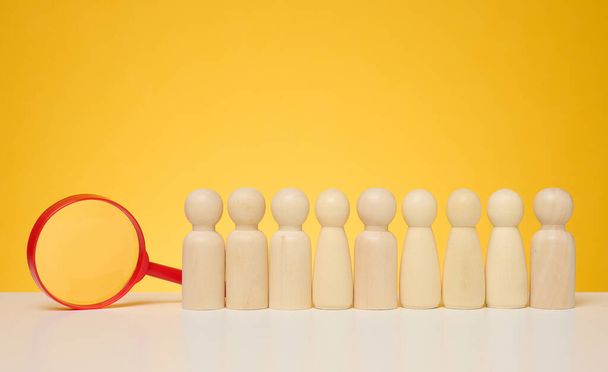 Wooden figures of men stand on a yellow background and a red plastic magnifying glass. Recruitment concept, search for talented and capable employees, career growth - Photo, Image