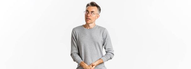 Image of annoyed middle-aged man rolling eyes, looking up, wearing sweater and glasses, standing over white background. - Photo, Image