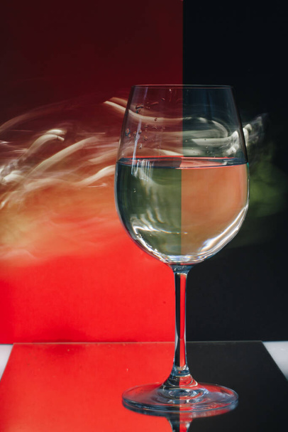 Натюрморт зі склянкою, наповненою водою і світловими лініями, намальованими навколо неї на барвистому червоно-чорному тлі, що створює ілюзію
. - Фото, зображення