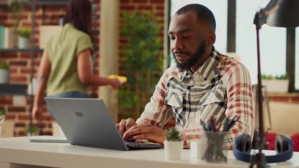 Mladý muž sedí doma a používá notebook, učí se účetní práci s firemními síťovými daty. Muž pracující na dálku a kontrolující informace o společnosti. Ruční snímek. - Záběry, video