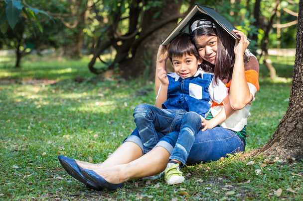 Mother protect her son with a book in park under the tree - Photo, Image