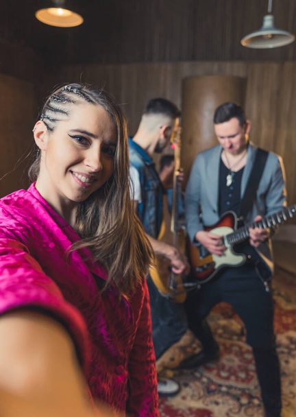 Selfie vertical tirada por morena caucasiana elegante funky que é vocalista em uma banda de rock. Dois outros membros da banda em segundo plano. Foto de alta qualidade - Foto, Imagem