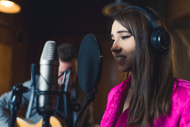 Singer új dalt vesz fel. Barna hajú kaukázusi énekesnő portréja, amint mikrofonnak énekel. Zenekari koncepció. Kiváló minőségű fénykép - Fotó, kép