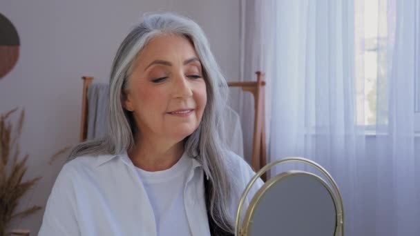Kaukasische lächelnd schöne alte Seniorin reifen alternden älteren Modell Frau mit grauen Haaren weiblich Blick auf Spiegel Reflexion Lächeln Blick auf Falten Gesichtshaut glatt natürliche Gesichtsschönheit Teint - Filmmaterial, Video