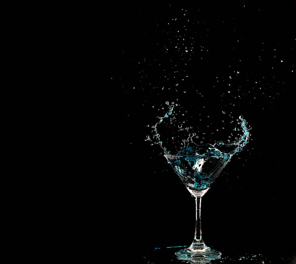 Blue Cocktail Glass with splashing water alcohol, Crystal Cocktail drink splatter splash in air and bubble from glass. Liquor Part freeze shot high speed over black background isolated - Photo, Image