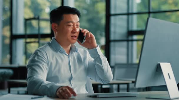 自信を持って大人40代のビジネスマンアジアの日本人男性コンサルタントは、オフィスの職場に座っている携帯電話の無線を話す5g接続遠くの携帯電話の呼び出しは、リモートでビジネスコンサルタントの職業を交渉 - 映像、動画