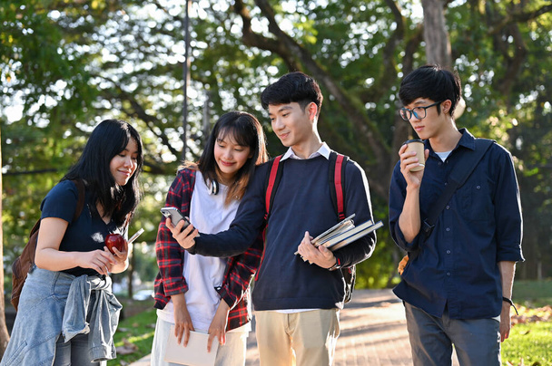 Ομάδα νεαρών Ασιατών φοιτητών απολαμβάνουν τη βόλτα στο πάρκο της πανεπιστημιούπολης μαζί μετά την ολοκλήρωση της τάξης. - Φωτογραφία, εικόνα