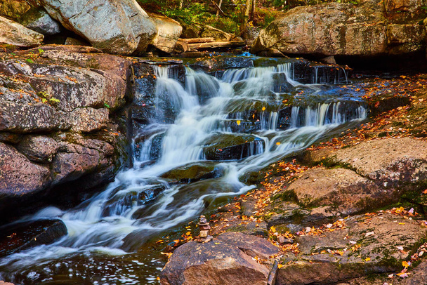 Изображение маленькой каскадной реки с камнями, покрытыми осенними листьями и крошечным стеком камней по краям - Фото, изображение