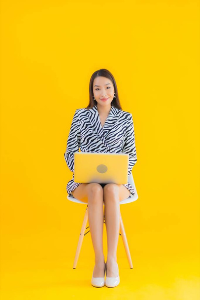 Портрет красивая молодая азиатская женщина использовать ноутбук на желтом изолированном фоне - Фото, изображение