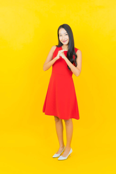 Portrait belle jeune femme asiatique porter robe rouge sourire avec action sur fond de couleur jaune - Photo, image