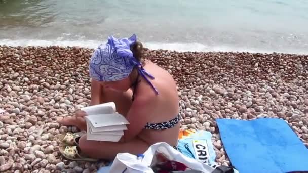 Женщина в платке читает книгу на пляже
 - Кадры, видео