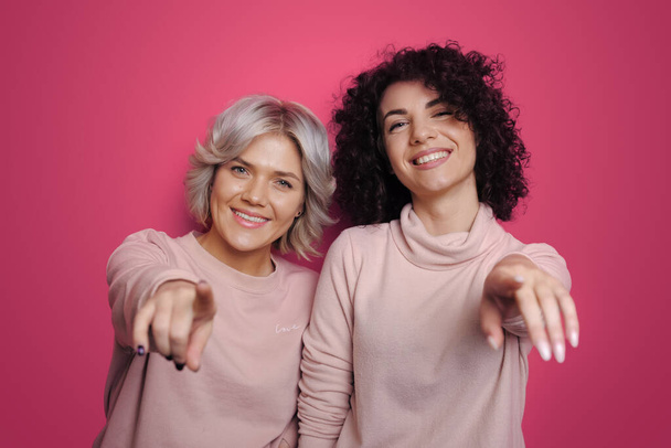 Image of happy two women friends having fun isolated over pink background. Looking camera pointing. Attractive beautiful girl. Excited cheerful. - Photo, Image