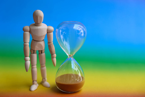 Wooden mannequin doll and hourglass on rainbow background - Photo, Image