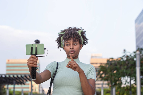 junge afrikanisch-amerikanische Frau spaziert durch die Stadt und überträgt live auf ihr Smartphone.. - Foto, Bild