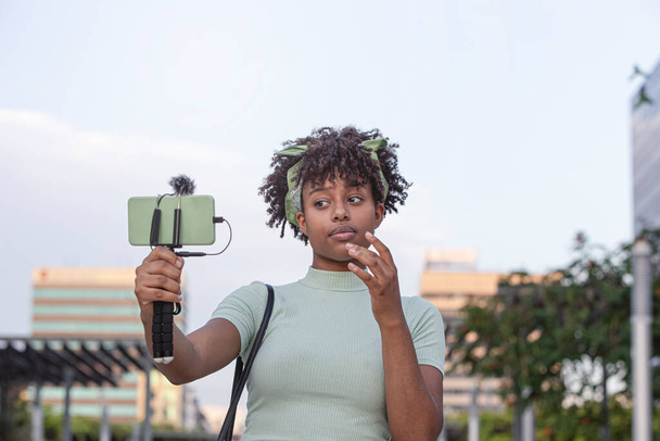 nuori afrikkalainen amerikkalainen nainen kävelee ympäri kaupunkia ja lähettää suorana älypuhelimellaan.Nuori bloggaaja käsite, kopioi tilaa. - Valokuva, kuva