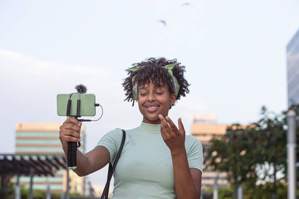 Nuoren afroamerikkalaisen naisen muotokuva suorana hänen älypuhelimellaan kävellessään kaupungin läpi. nuori bloggaaja käsite, kopioi tilaa. - Valokuva, kuva