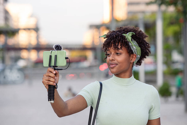 Πορτρέτο της νεαρής Αφροαμερικανής γυναίκας ζωντανά streaming, ενώ το περπάτημα γύρω από την πόλη. νέα έννοια blogger, αντιγραφή χώρου. - Φωτογραφία, εικόνα