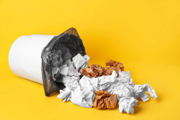 Umgekippter Mülleimer mit zerknülltem Papier auf gelbem Hintergrund - Foto, Bild