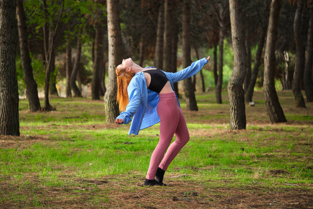 Redhead young woman practicing contemporary dance in a forest. Dancer in nature. - Photo, Image