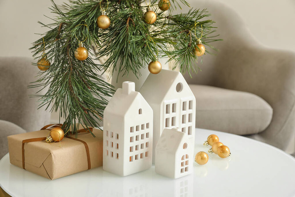 Váza s vánočními větvemi, míčky a držáky svíček ve tvaru domu na stole v obývacím pokoji - Fotografie, Obrázek
