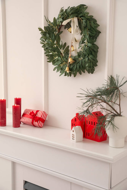 Vase with Christmas branches, house shaped candle holders and gift on mantelpiece in room - Photo, Image