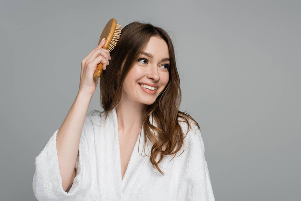 iloinen nuori nainen harjaamalla kiiltävät ja terveet hiukset katsellen pois eristetty harmaa - Valokuva, kuva