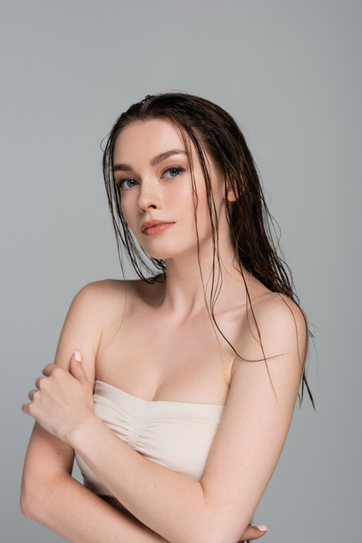 pretty and young woman with wet hair and bare shoulders looking at camera isolated on grey  - Foto, Imagen