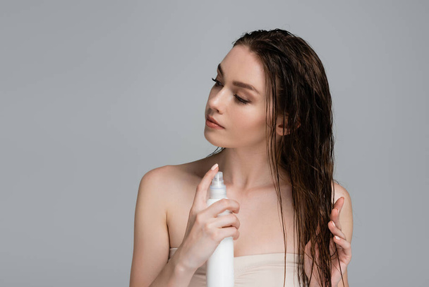 pretty young woman with bare shoulders applying treatment product on wet hair isolated on grey  - Foto, Bild