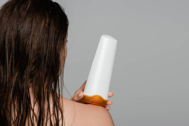 濡れた髪をした若い女性の背中を灰色に隔離されたシャンプーで瓶を持っている  - 写真・画像