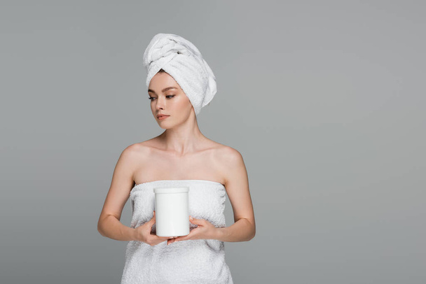 young woman with white towel on head holding jar with hair mask isolated on grey  - Foto, Imagem