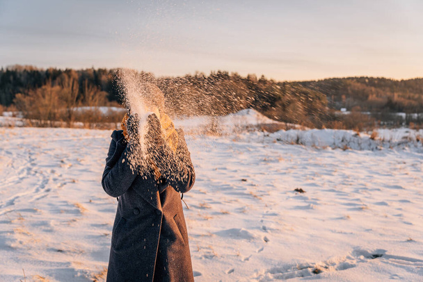 Kobieta z zamkniętą twarzą rzuca śnieg rękami na pokrytym śniegiem polu. - Zdjęcie, obraz