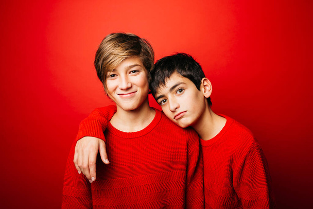 Dois meninos pré-adolescentes, vestindo uma camisola vermelha, abraçando sobre um fundo vermelho - Foto, Imagem