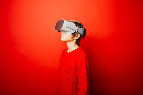 Vorpubertärer Junge in Rot vor rotem Hintergrund, der Videospiele mit Virtual-Reality-Brille spielt - Foto, Bild