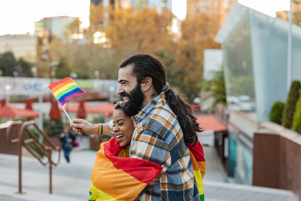 Diversas personas caminando en el desfile del Orgullo con la bandera del arco iris como símbolo del mes del Orgullo. pareja de diversos amigos caminar felizmente con banderas lgbt - Foto, imagen