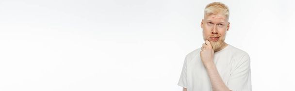 hombre albino pensativo en camiseta tocando la barba mientras piensa en blanco, bandera - Foto, imagen