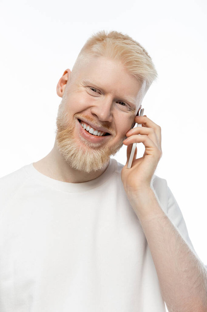 šťastný albín muž v tričku mluví na smartphone a usmívá izolované na bílém  - Fotografie, Obrázek