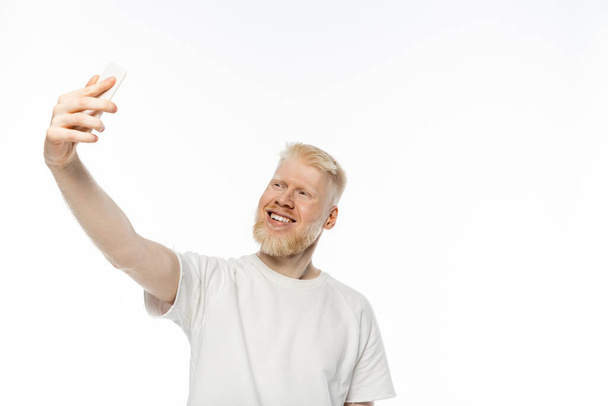 cheerful albino man in t-shirt taking selfie on smartphone on white background - Foto, Bild
