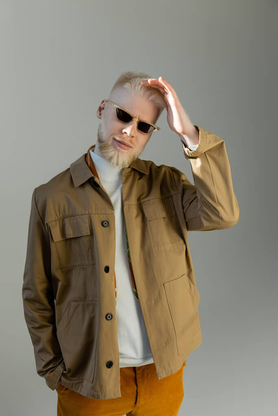 smiling albino man in stylish sunglasses and shirt jacket isolated on grey - Photo, image