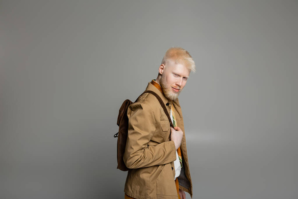 homme barbu albinos veste chemise élégante et écharpe en soie posant avec sac à dos isolé sur gris - Photo, image