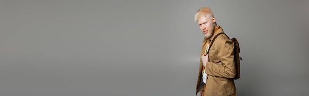 бородатый альбинос мужчина в стильной рубашке куртка позирует с рюкзаком изолированы на сером, баннер  - Фото, изображение