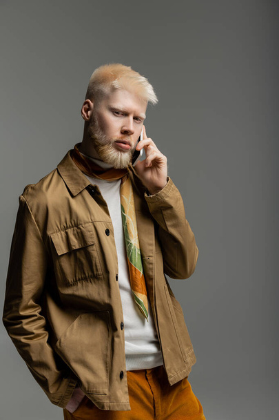 homem albino barbudo em camisa jaqueta falando no smartphone isolado no cinza  - Foto, Imagem