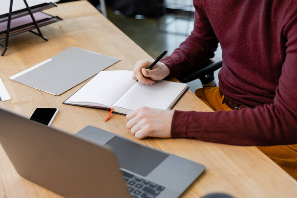 обрезанный вид бизнесмена, пишущего на ноутбуке рядом с устройствами на столе  - Фото, изображение