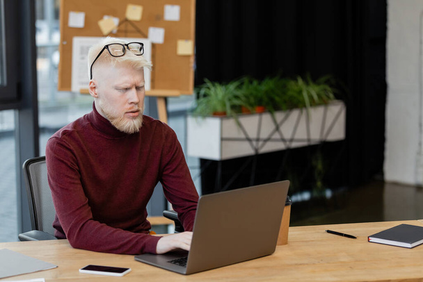 bearded albino businessman using laptop near smartphone with blank screen in office  - Foto, afbeelding