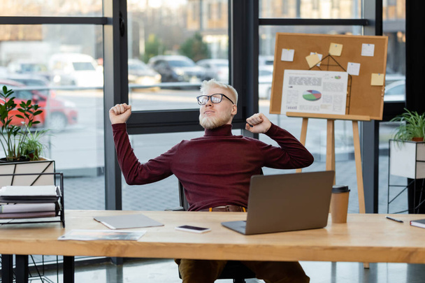 bearded albino businessman in glasses stretching near gadgets in office - Photo, Image