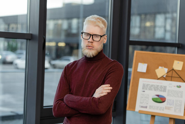 vousatý albín obchodník v brýlích se zkříženýma rukama v kanceláři - Fotografie, Obrázek