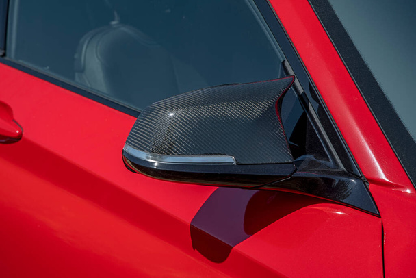 Közelkép egy piros autó fekete oldalsó szén-dioxid tükréről, amit napfény világít. - Fotó, kép